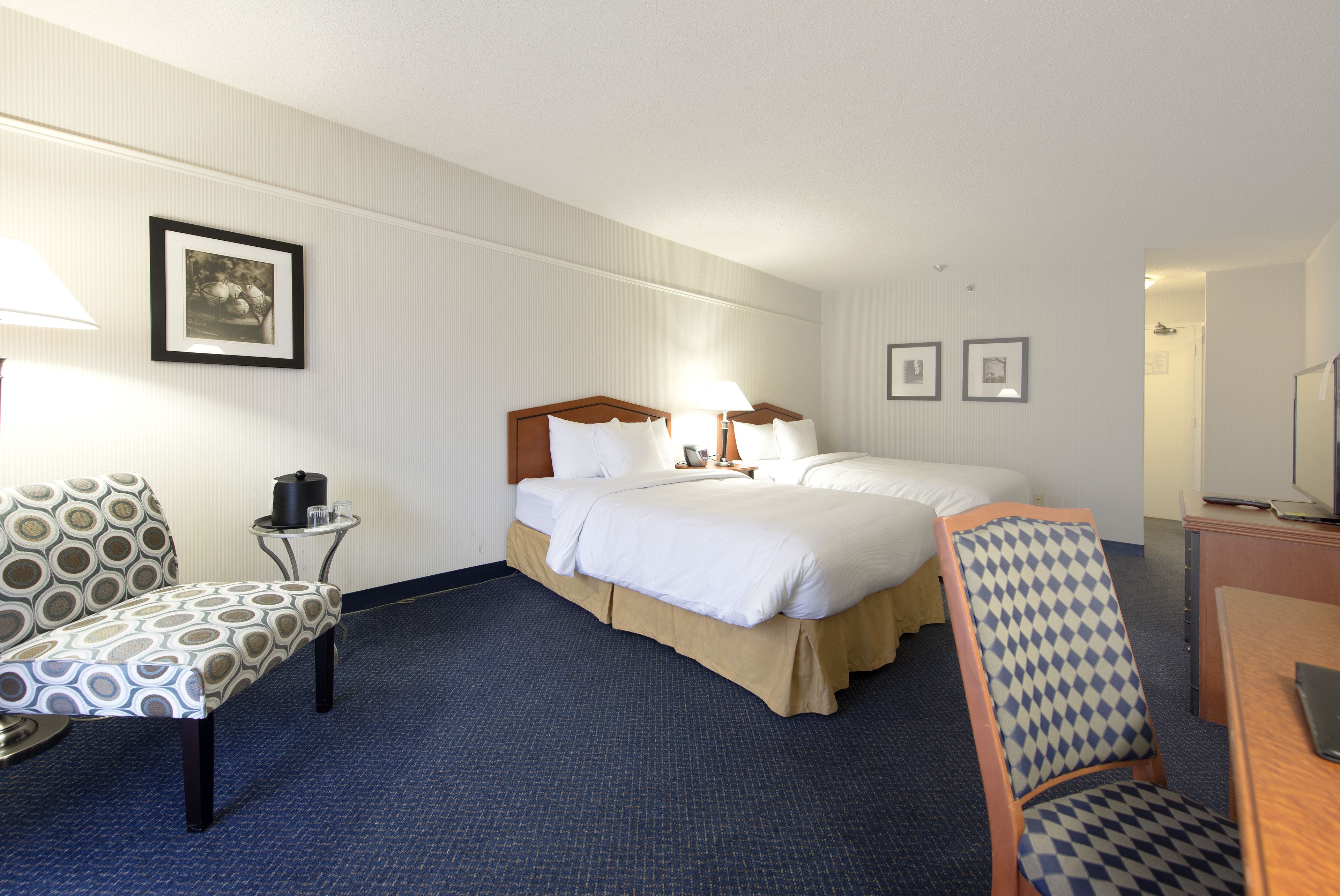 A hotel room with a bed, two chairs, a desk, and a lamp.