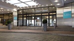 Une entrée d’hôtel moderne avec des portes en verre, une enseigne et des plantes en pot.