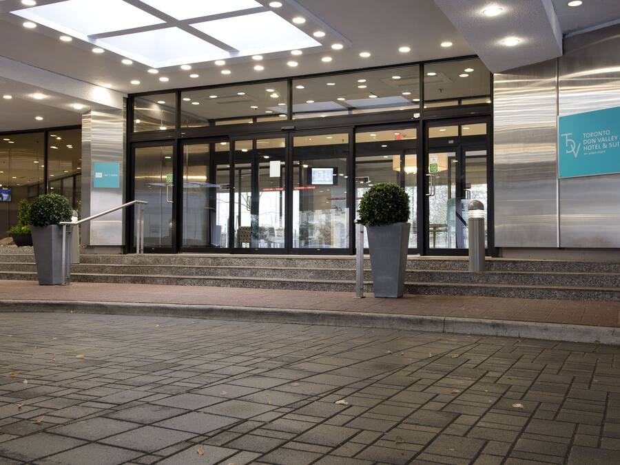 A modern hotel entrance with glass doors, a signboard, and potted plants.