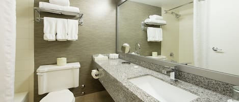 Une salle de bain moderne avec un comptoir en granit, un lavabo blanc, des toilettes et un miroir.