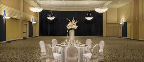 Un salón de banquetes con mesas redondas dispuestas para eventos, un gran centro de mesa floral y candelabros.