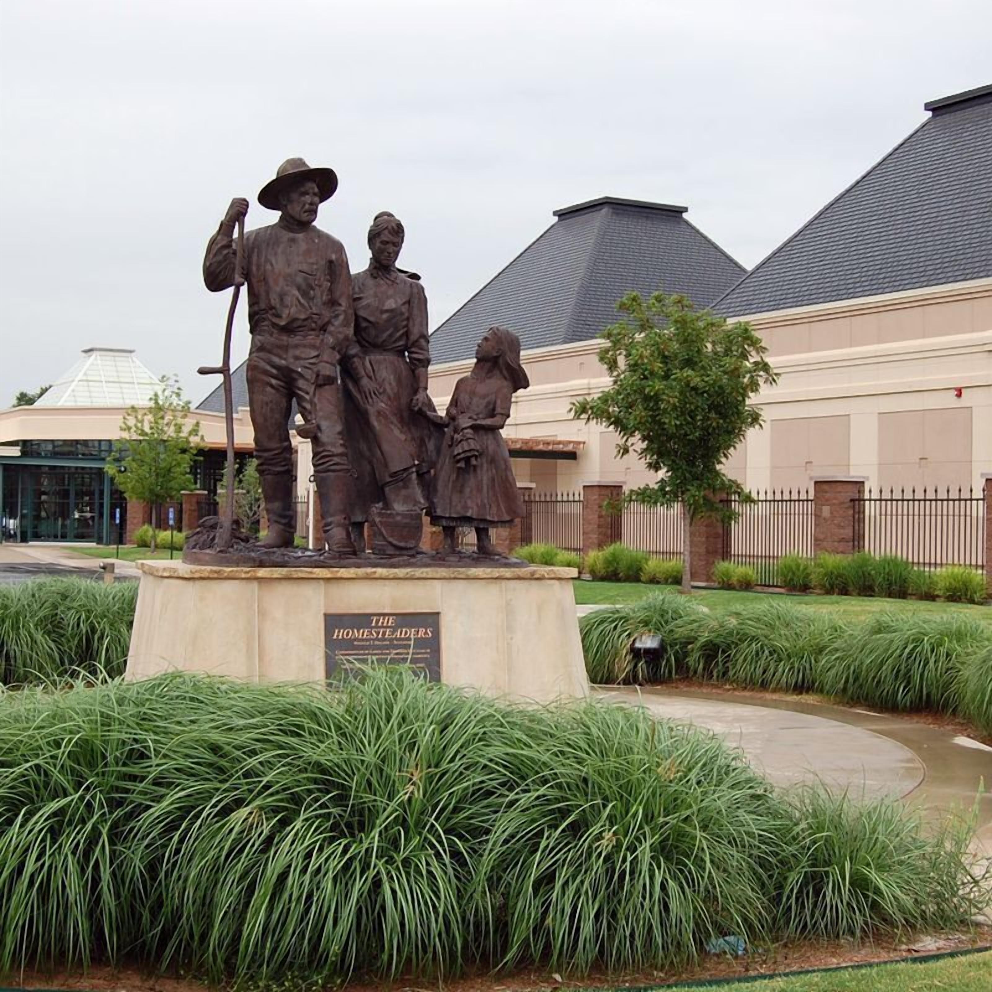 A bronze statue of a family in a landscaped area with a building in the background.