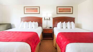 A hotel room with two beds, a nightstand, a lamp, and two framed pictures on the wall.