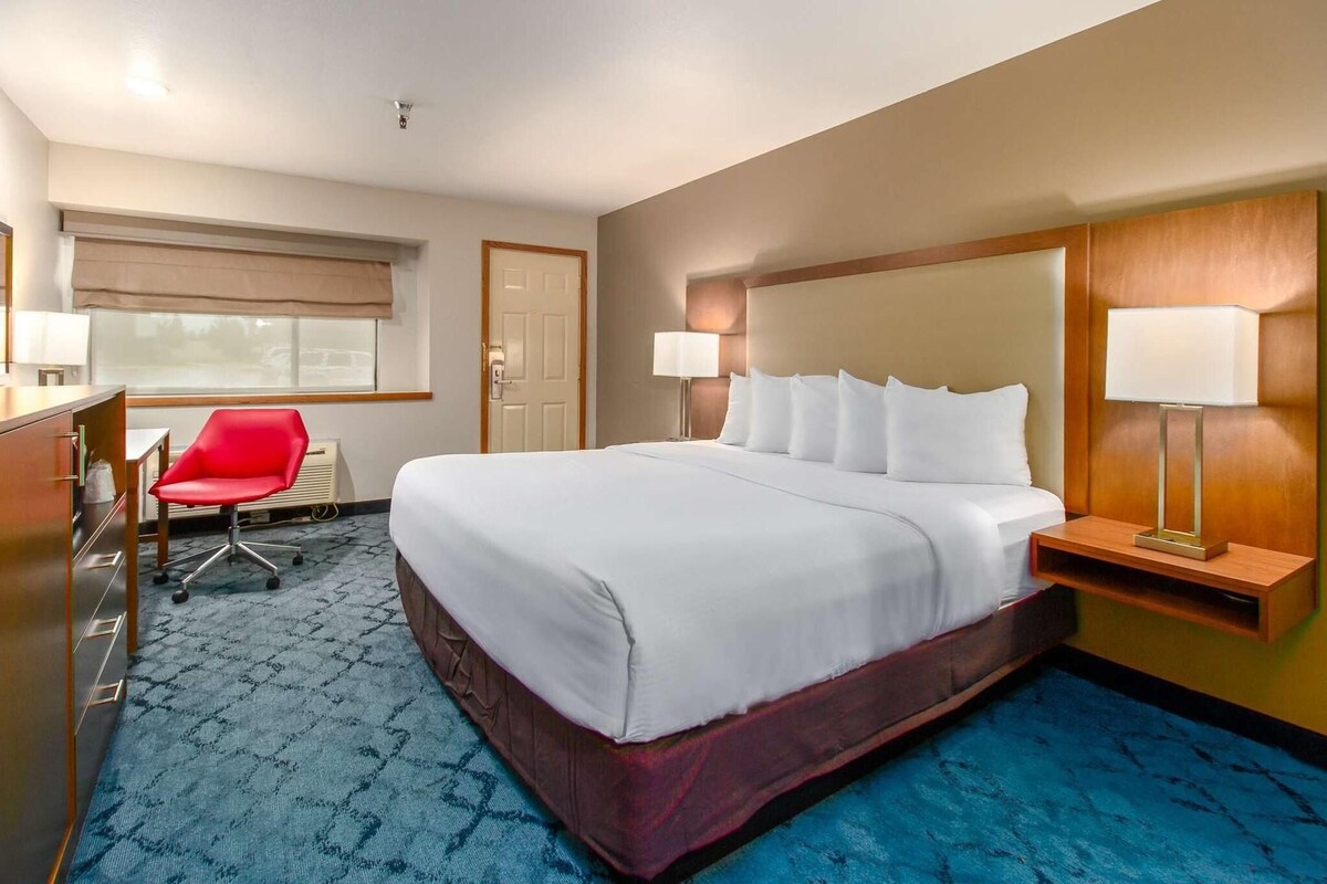 A hotel room with a large bed, a desk with a chair, a lamp, and a window with a view.