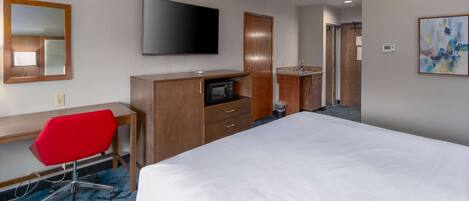 A hotel room with a bed, a desk with a red chair, a television, a microwave, and a bathroom visible in the background.