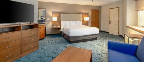 A hotel room with a large bed, a TV, a desk, and a blue sofa.