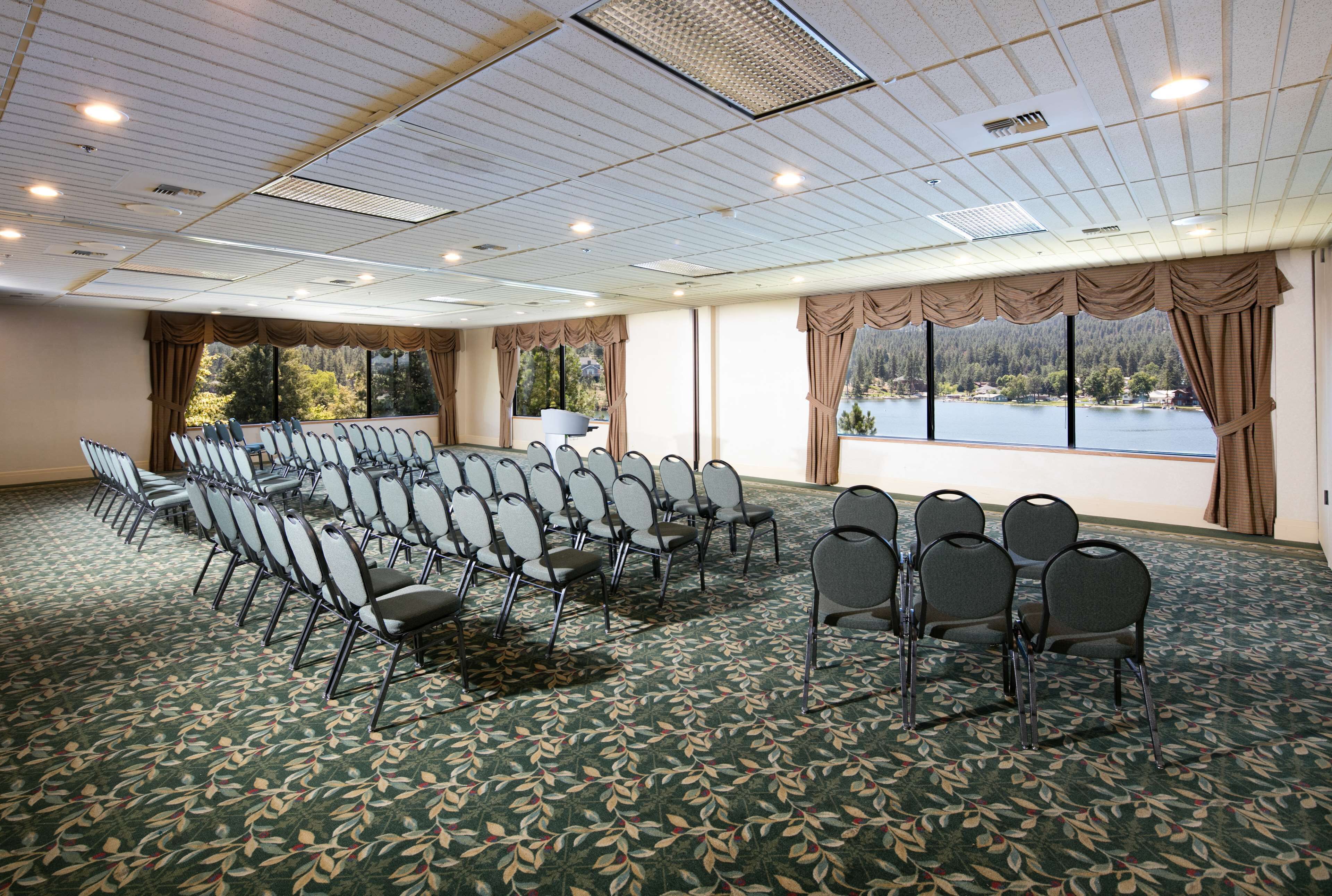 Une salle de conférence avec des rangées de chaises, de grandes fenêtres avec des rideaux et une vue sur un lac.