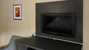 A modern living room with a flat-screen TV mounted on a dark wood panel, a gray sofa, and a framed picture on the wall. - Days Inn by Wyndham Charlotte Northlake (Charlotte)