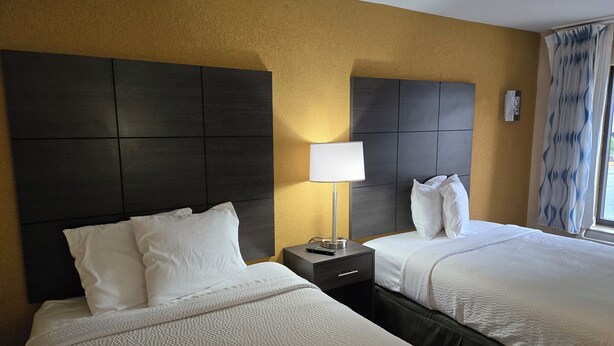 A hotel room with two beds, a nightstand, a lamp, and a window with curtains. - Days Inn by Wyndham Charlotte Northlake (Charlotte)