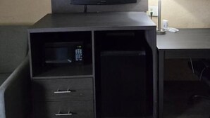 A hotel room with a dark wooden TV stand, a flat-screen TV, a lamp, and a small refrigerator. - Days Inn by Wyndham Charlotte Northlake (Charlotte)