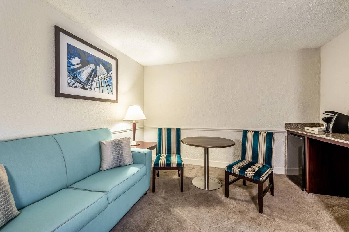 A room with a blue sofa, striped chairs, a small round table, a lamp, and a framed picture on the wall.