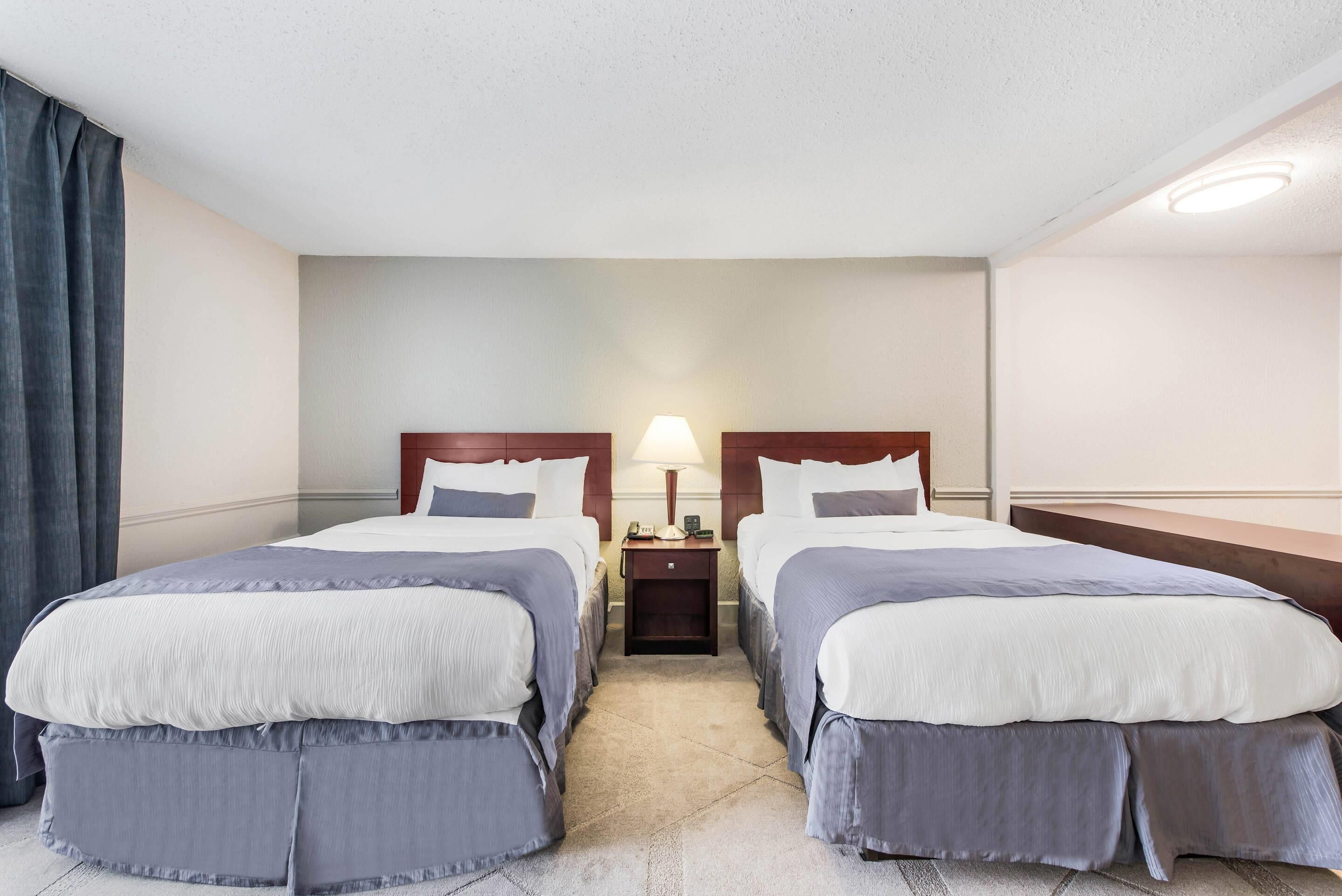 Une chambre d’hôtel avec deux lits, une table de chevet avec une lampe et une fenêtre avec des rideaux.