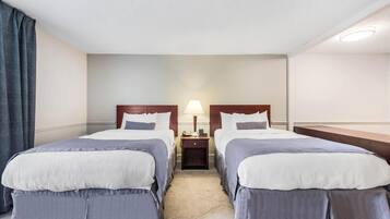 Une chambre d’hôtel avec deux lits, une table de chevet avec une lampe et une fenêtre avec des rideaux.