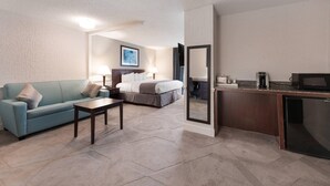 A hotel room with a sofa, a bed, a desk, and a kitchenette.