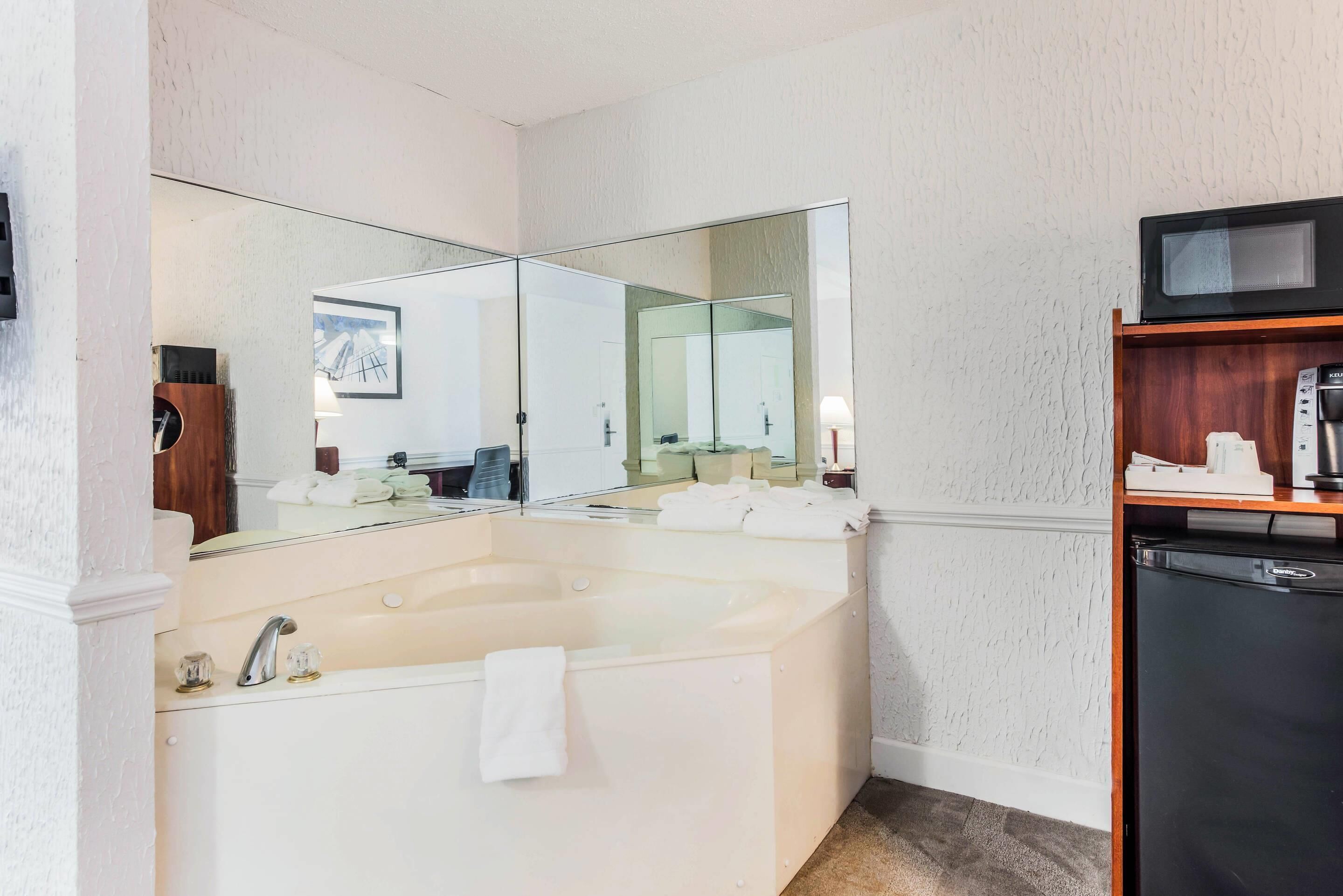 Une salle de bain avec un grand miroir, une baignoire, un lavabo et un réfrigérateur noir.