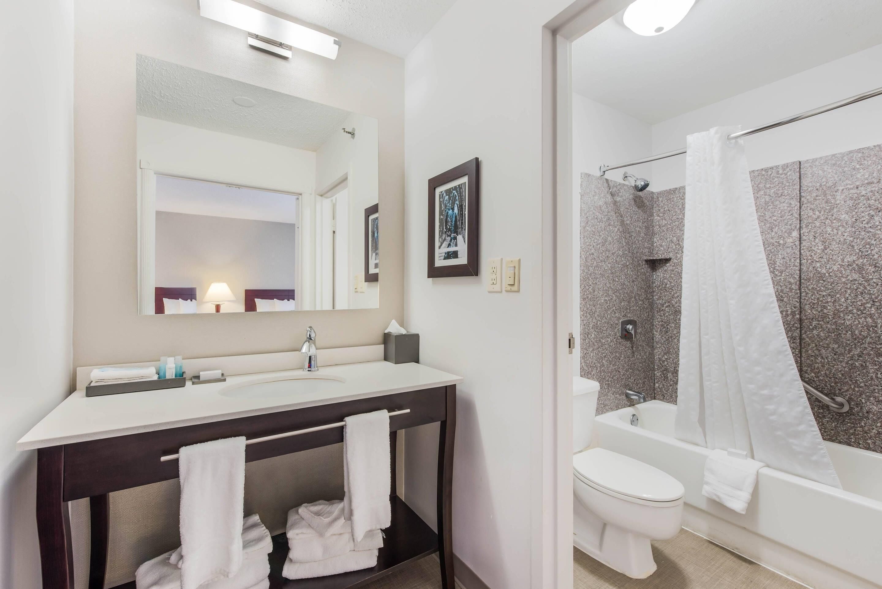A modern bathroom with a white sink, mirror, and toilet, a shower with a curtain, and towels on the counter.