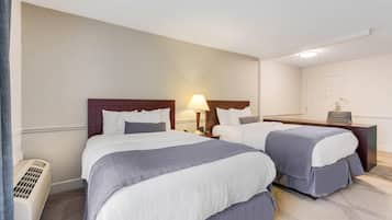 Habitación de hotel con dos camas, una mesita de noche con lámpara, un calentador y un pequeño escritorio con silla.