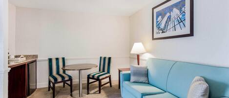 Ein Zimmer mit einem hellblauen Sofa, gestreiften Stühlen, einem runden Tisch, einer Lampe und einem gerahmten Bild an der Wand.