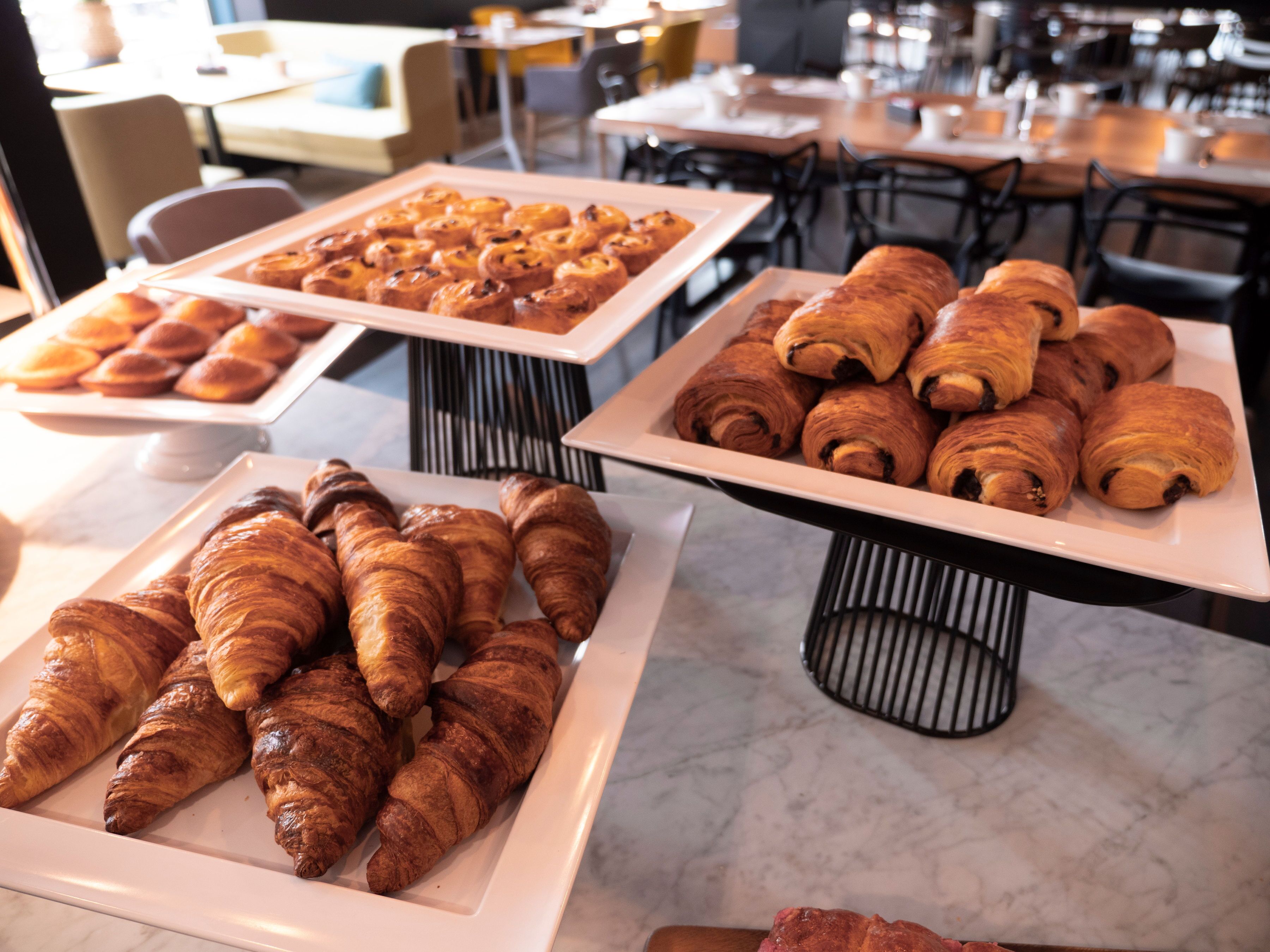 Buffet com diversos produtos de panificação, incluindo pastelaria e pão, dispostos em travessas brancas.