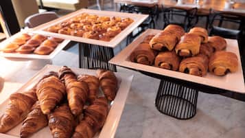 Buffet com diversos produtos de panificação, incluindo pastelaria e pão, dispostos em travessas brancas.