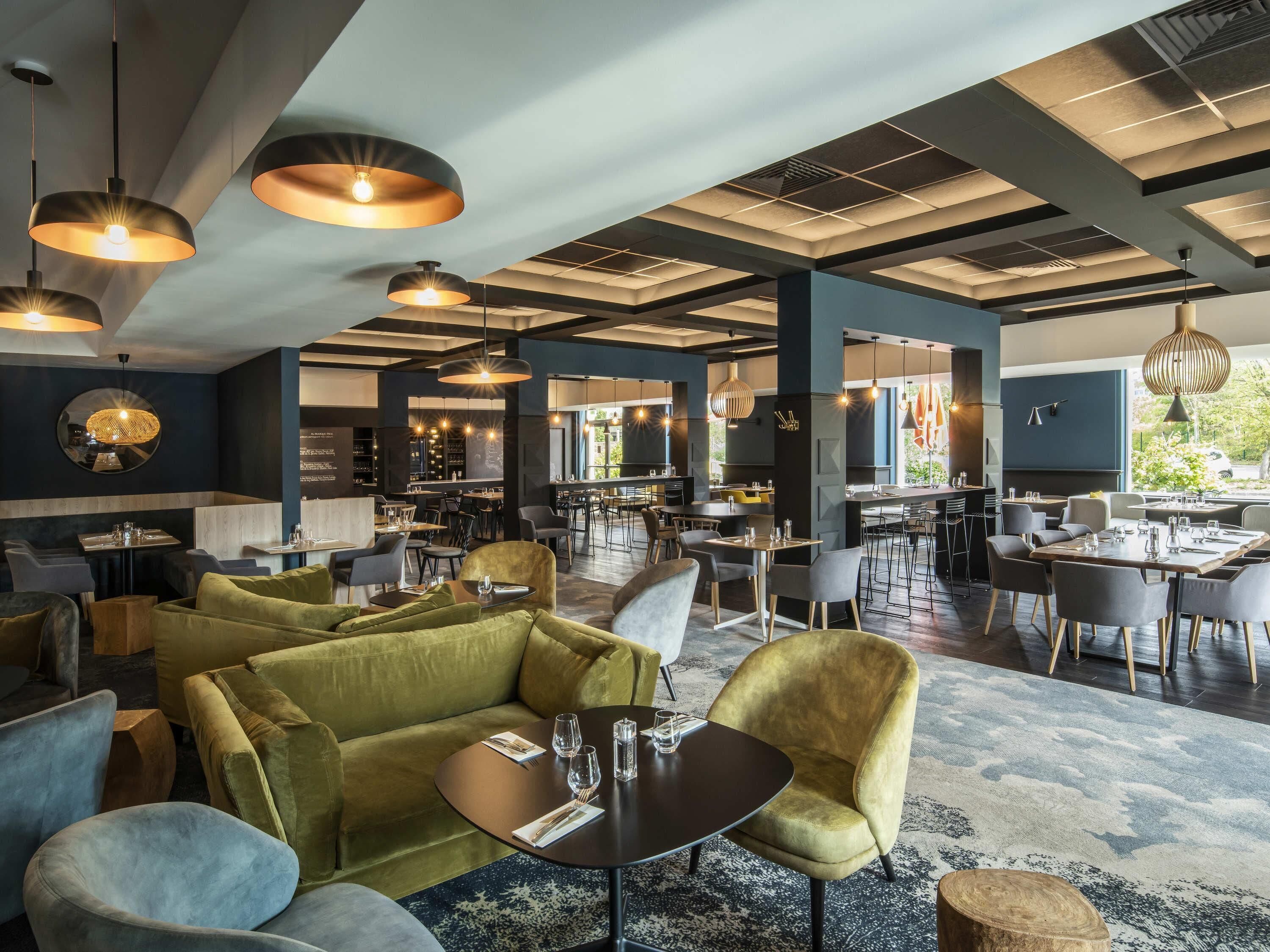 A spacious restaurant with high ceilings, pendant lighting, and a mix of seating arrangements including sofas and tables.