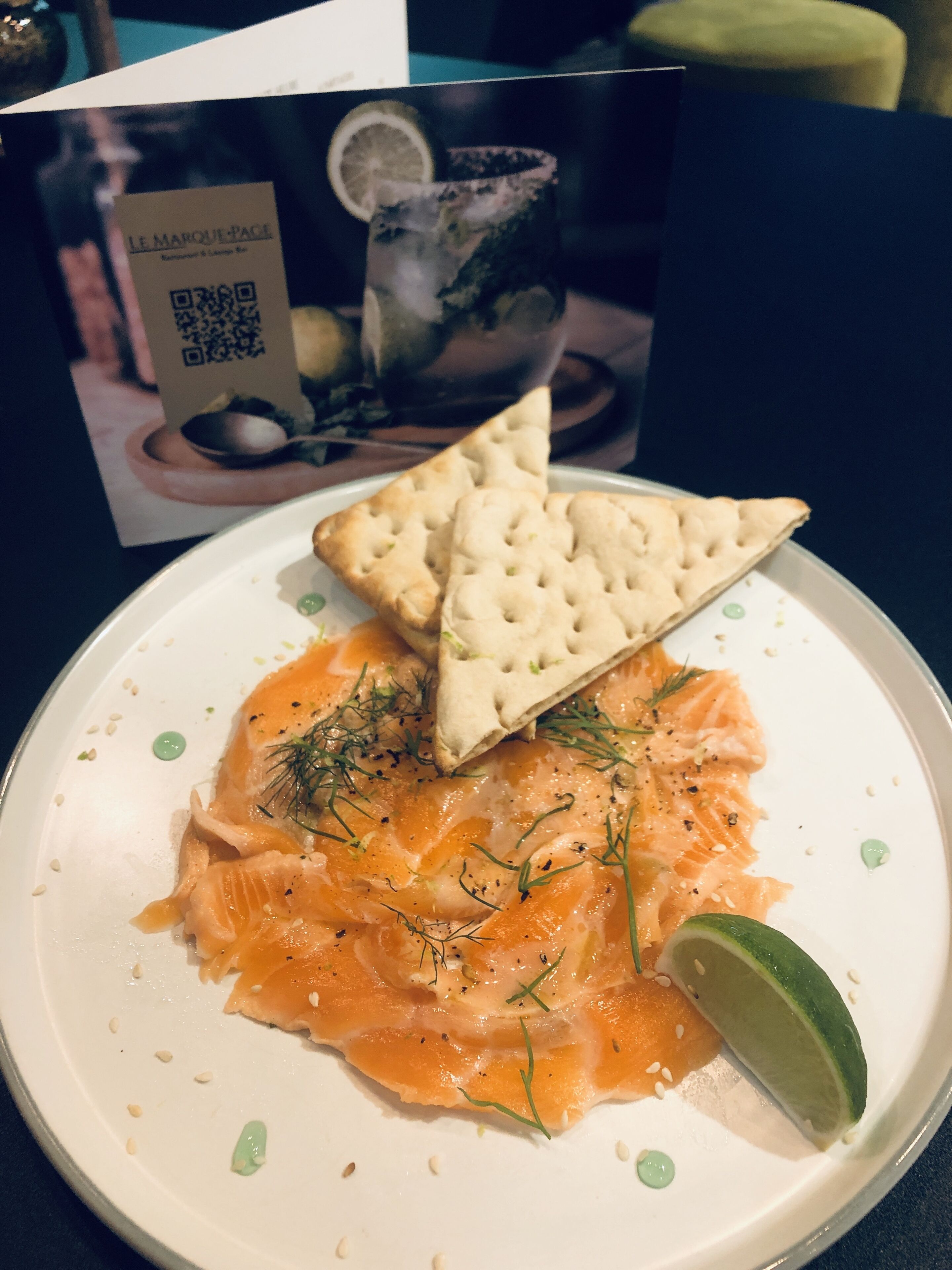 Une assiette de saumon fumé, servie avec des crackers et un quartier de citron vert.