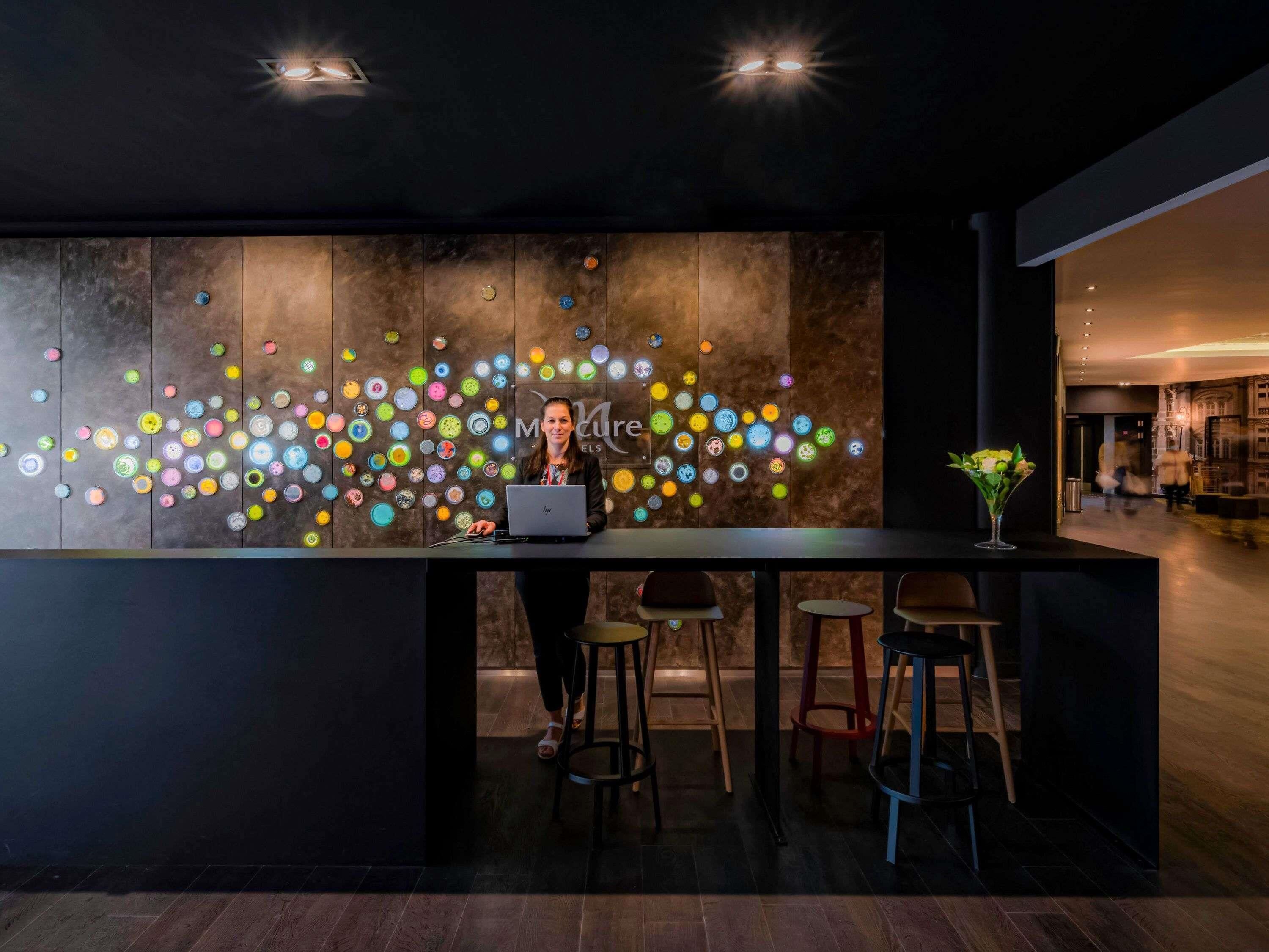 Un espace bar moderne avec un ordinateur portable posé sur le comptoir, des tabourets et un mur décoratif orné de motifs circulaires.