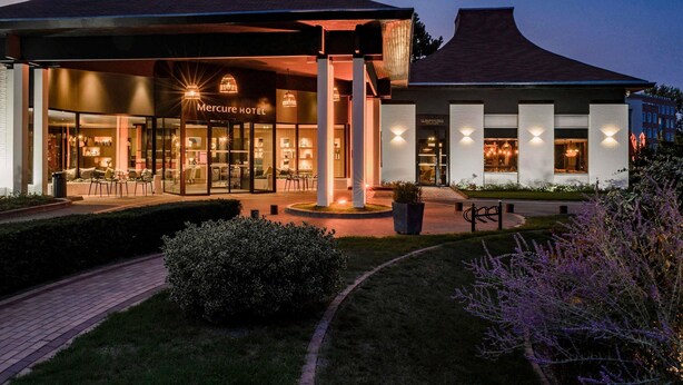 A hotel with a modern design, featuring a covered outdoor seating area and a well-lit entrance. - Mercure Lille Marcq en Baroeul (Marcq-en-Baroeul)