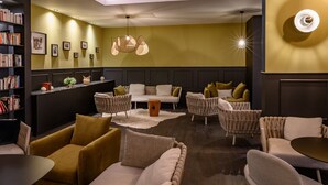 A modern lounge area with sofas, a coffee table, and a bookshelf. - Mercure Lille Marcq en Baroeul (Marcq-en-Baroeul)