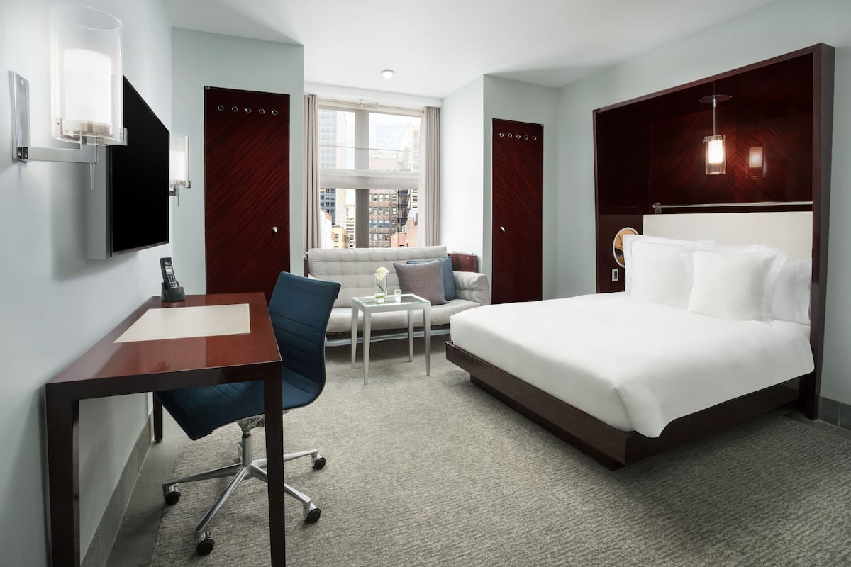Quarto de hotel com cama, escrivaninha, cadeira, mesinha e sofá.
