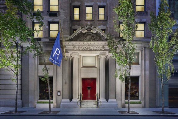 A grand entrance with a red door, a blue flag with a 'P' logo, and a building facade with classical architecture.