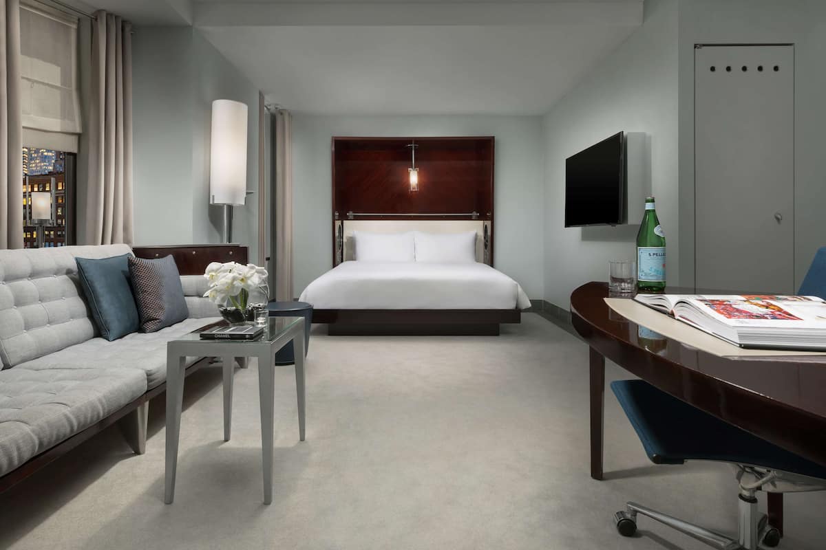 Quarto de hotel moderno com cama, sofá, escrivaninha e televisão.