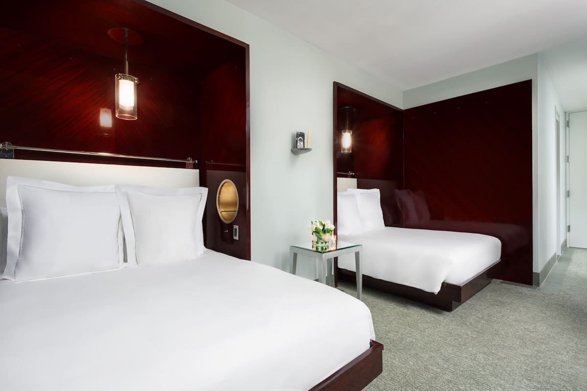 Quarto de hotel com duas camas, uma mesinha com um vaso de flores e um espelho na parede.