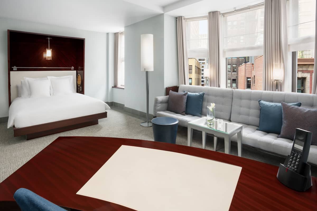 Quarto de hotel com cama, sofá, mesa de centro, abajur e telefone.