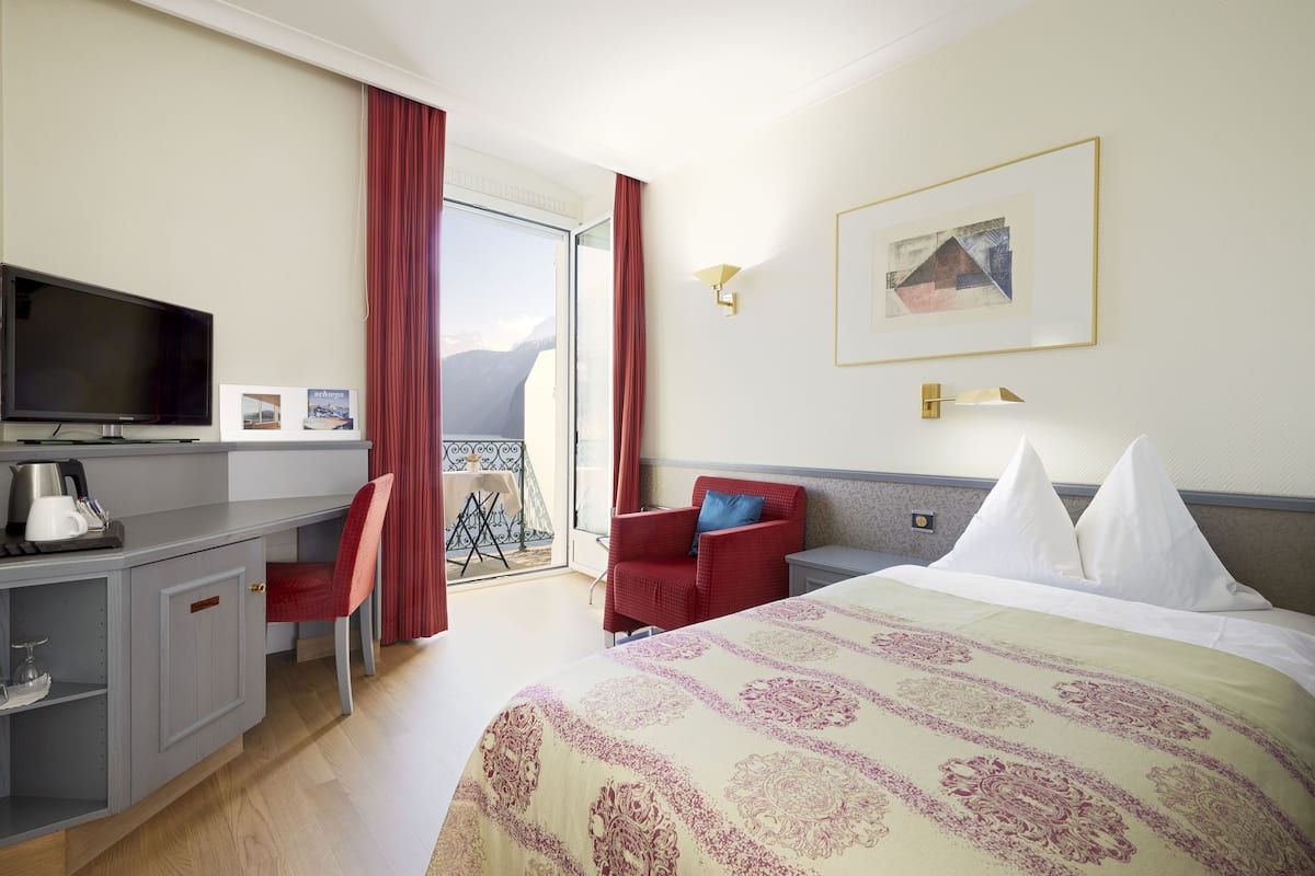 Une chambre d’hôtel avec un lit, un bureau avec une télévision, une chaise et une vue sur les montagnes par la fenêtre.