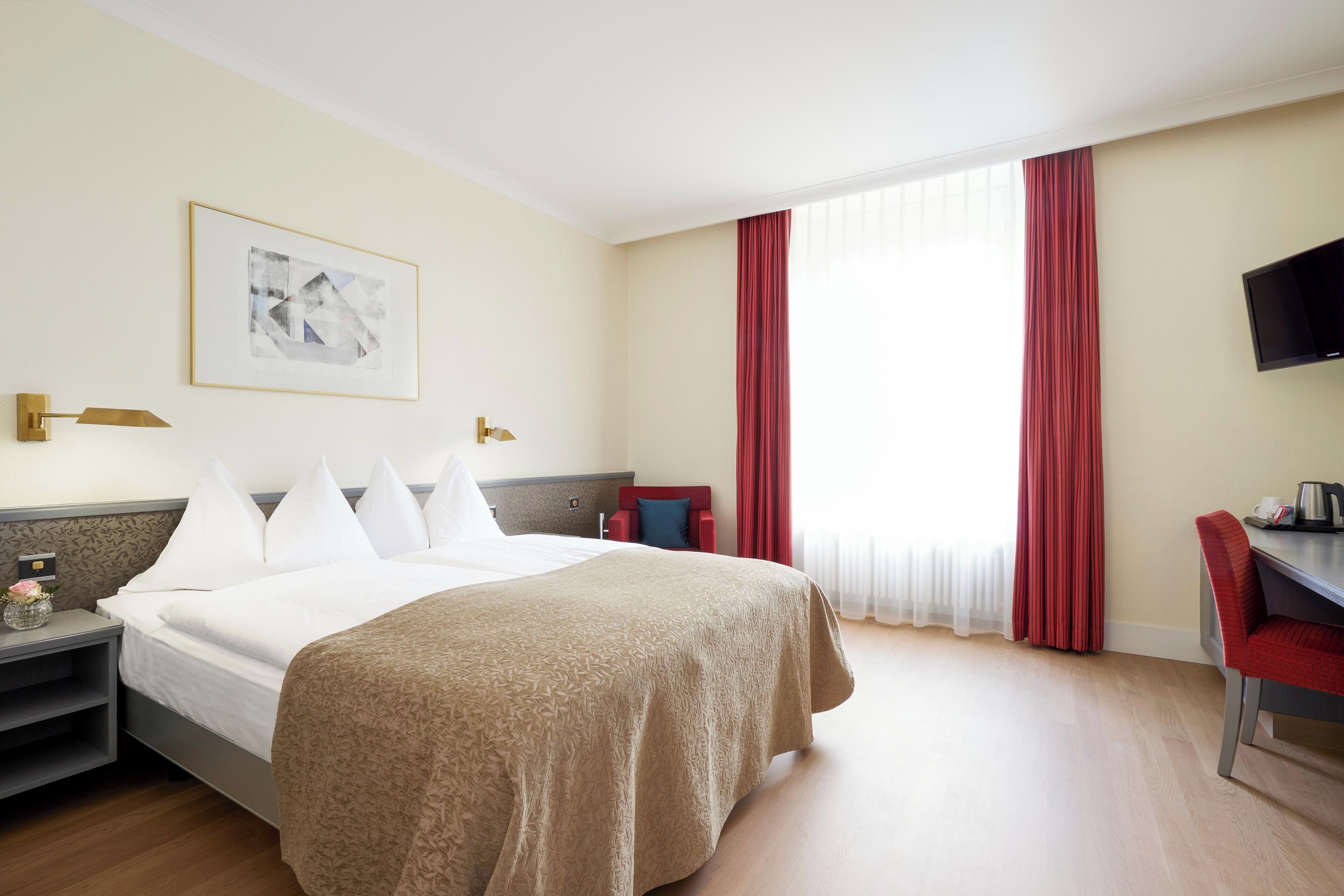 Una habitación de hotel con una cama grande, un escritorio, una silla, un televisor y una ventana con cortinas.