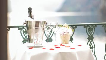 Una mesa con una botella de champán, dos copas y un ramo de flores en un balcón con barandilla.