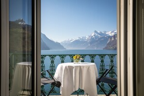 A balcony with a table and chairs, overlooking a lake and mountains. - Seehotel Waldstaetterhof Swiss Quality (Ingenbohl)