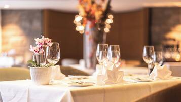 A dining table set with white tablecloths, wine glasses, and a vase with flowers.