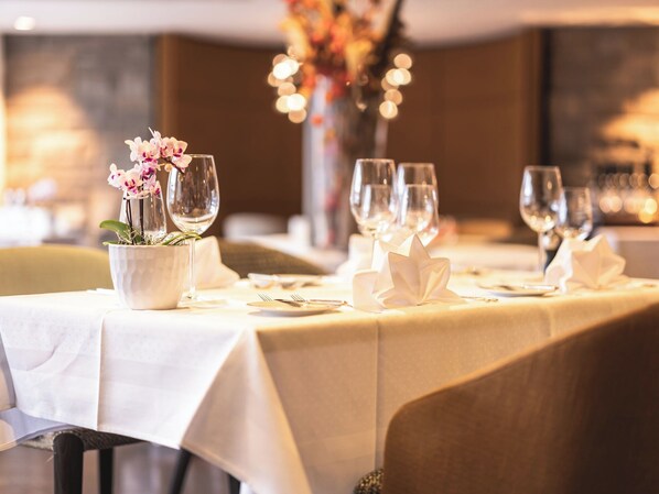 Una mesa de comedor decorada con manteles blancos, copas de vino y un florero con flores.