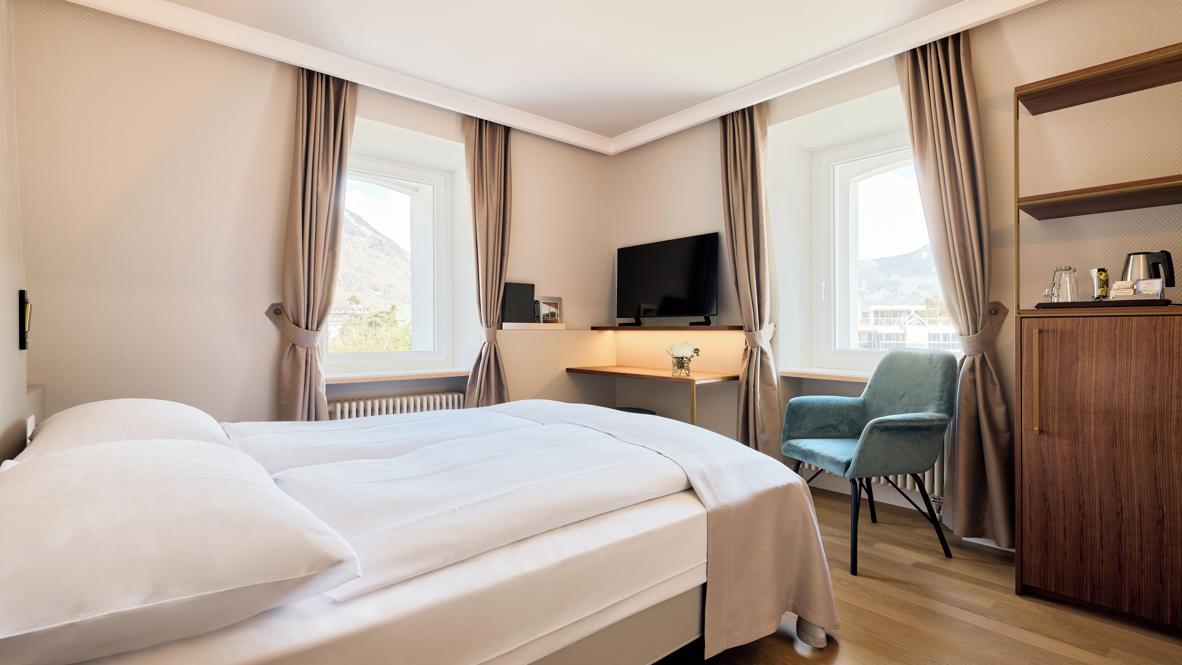A hotel room with a bed, a desk, a chair, a TV, and a wardrobe.