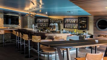 A modern bar area with a long counter, multiple stools, and a variety of bottles.