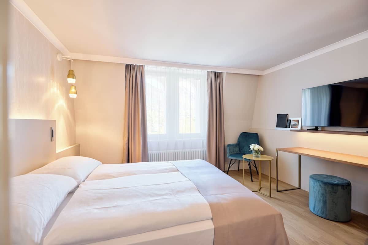 Une chambre d’hôtel équipée d’un lit, d’un bureau, d’une chaise, d’une télévision et d’une fenêtre avec des rideaux.