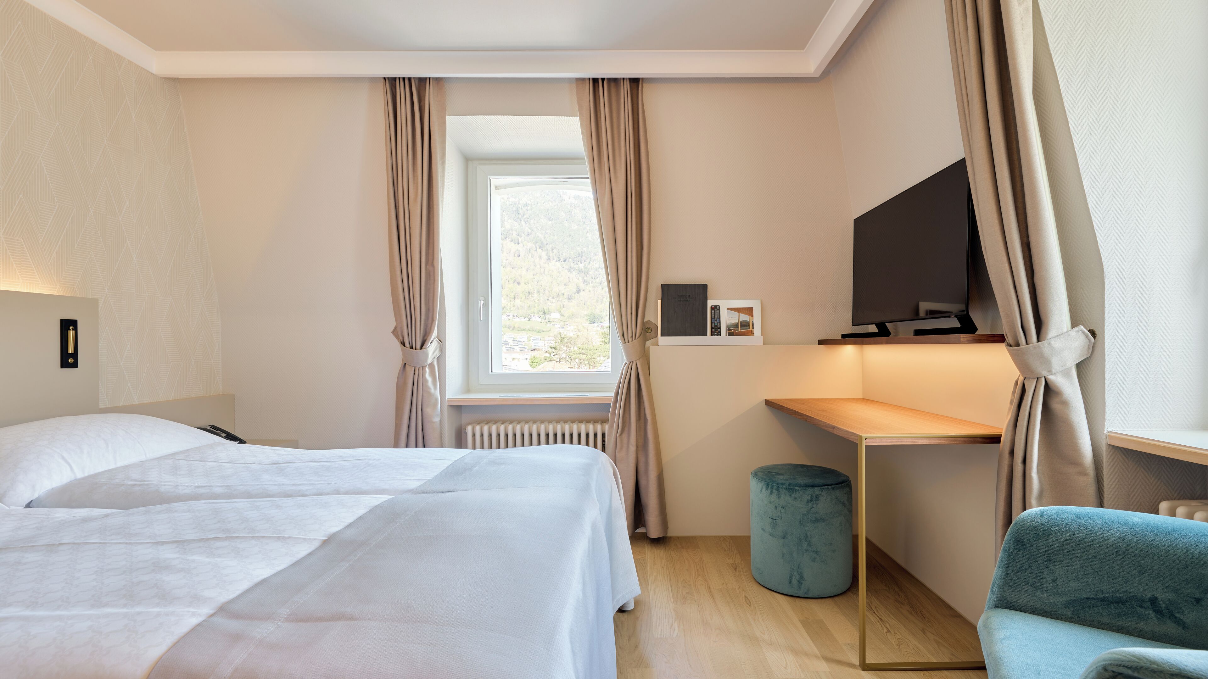 Habitación de hotel con cama, escritorio, silla, televisor y ventana con cortinas.