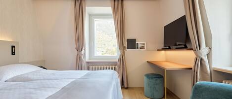 Habitación de hotel con cama, escritorio, silla, televisor y ventana con cortinas.