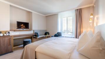 A hotel room with a bed, a desk, a television, and a window with curtains.