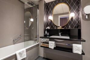 Un bagno moderno con doccia vetrata, un mobile lavabo nero con specchio dorato e un asciugamano bianco sul bordo della vasca.