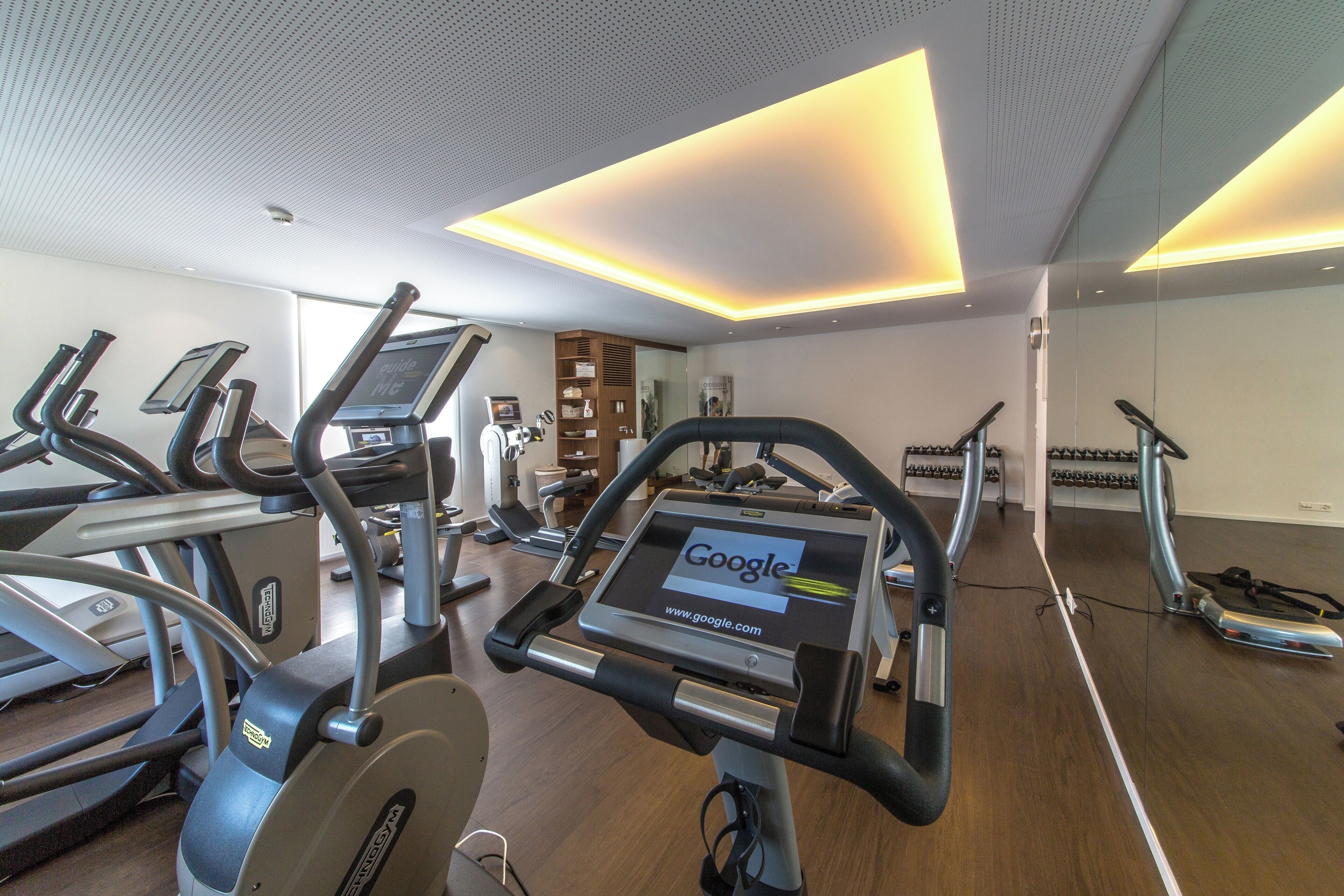 A gym with treadmills, stationary bikes, and a mirrored wall.