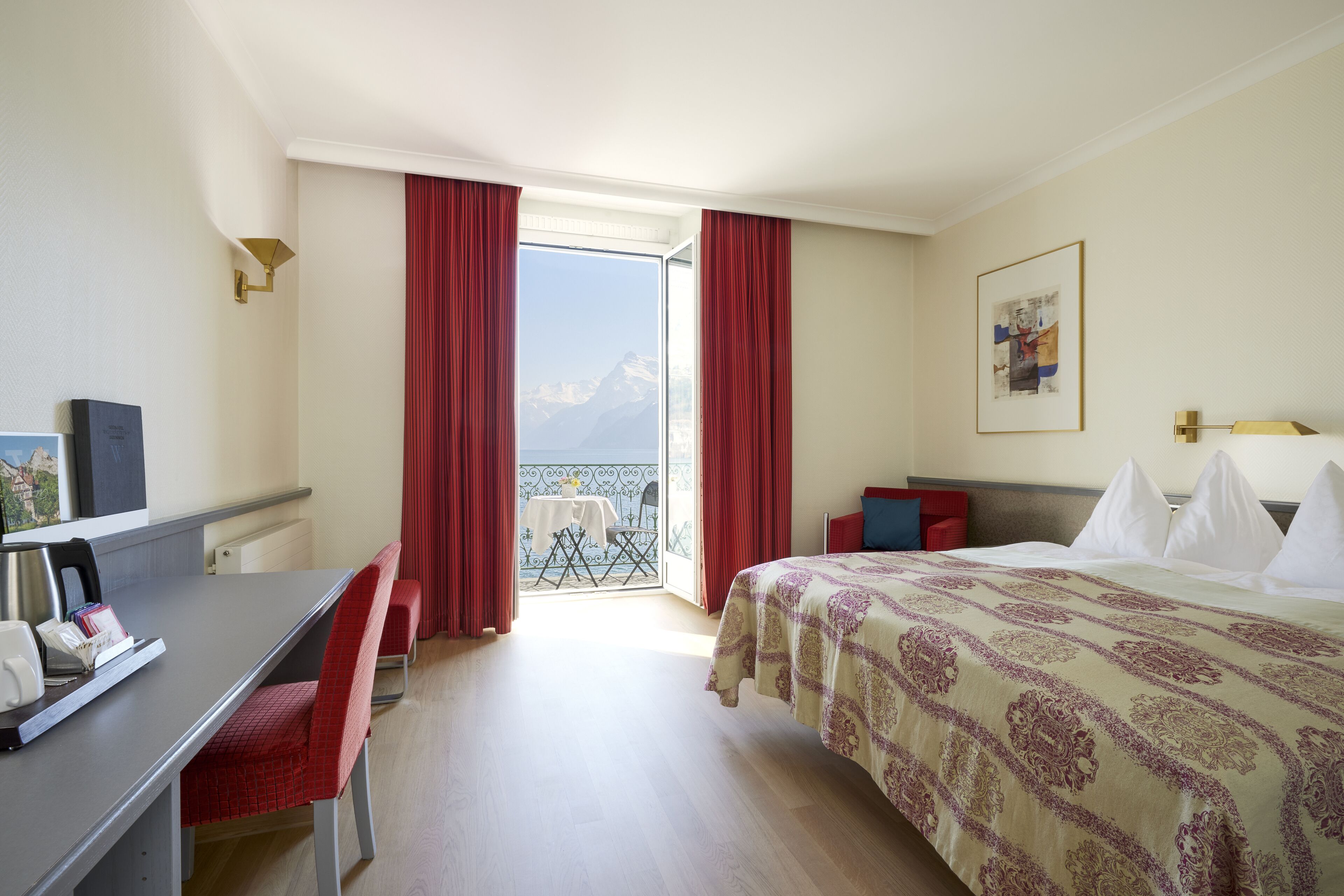 Ein Hotelzimmer mit Bett, Schreibtisch und Blick auf Berge durch das Fenster.