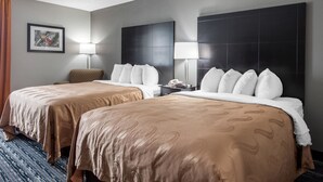 A hotel room with two beds, a large dark headboard, a framed picture on the wall, and a lamp on the nightstand. - Quality Inn & Suites Brownsburg - Indianapolis West (Brownsburg)